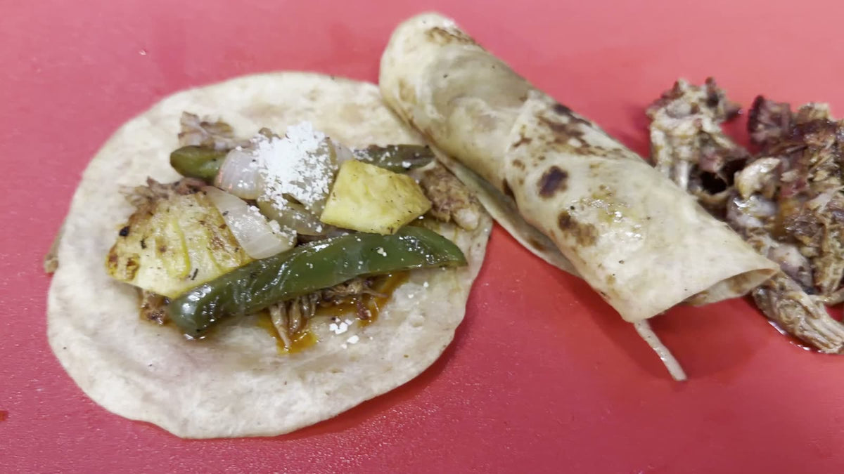 Smoked al pastor pulled pork taco topped with grilled pineapple, jalapenos, onions and crumbled cheese